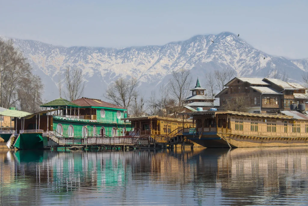 Kashmir Trip Cost from India (2026–27): What a 7-Day Trip Really Costs a Couple 2 Wooden houseboats on Dal Lake in Srinagar with snow on the mountains behind